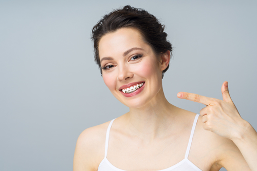 A young woman with braces on her teeth, smiles and points to the copy space with a hand gesture,