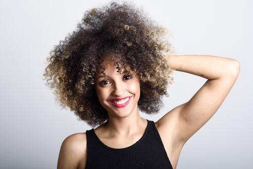 Young black woman with afro hairstyle laughing. Girl wearing black clothes. Studio shot.