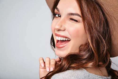 Portrait of young stylish laughing girl model in gray casual summer clothes in brown hat with natural makeup isolated on gray background. Looking at camera and winking