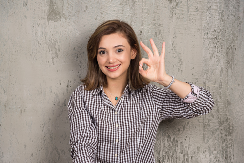 Portrait of a cute young woman showing ok sign with fingers and looking to camera . High quality photo