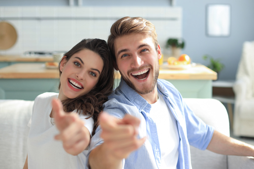 Portrait of cute young couple pointing and laughing, sitting in sofa