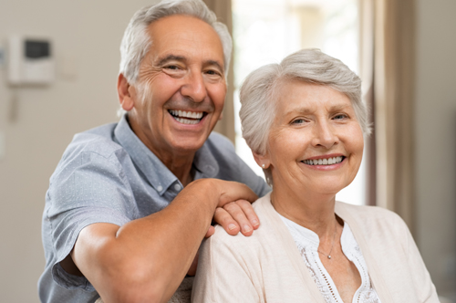 Portrait of happy healthy senior couple at home. Romantic old couple sitting together on sofa while looking at camera. Cheerful elderly wife and husband enjoying life after retirement.