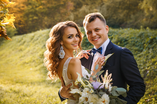 Elegant curly bride and stylish groom hugging on the green meadow