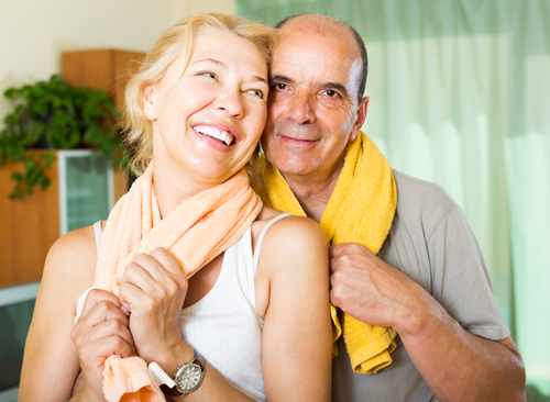 Happy mature couple with towels smiling after training at home