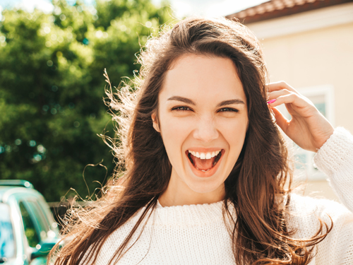 Closeup portrait of beautiful smiling brunette model. Trendy girl posing in the street background. Funny and positive woman having fun outdoors