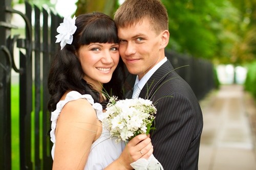 Bride and groom standing together in park