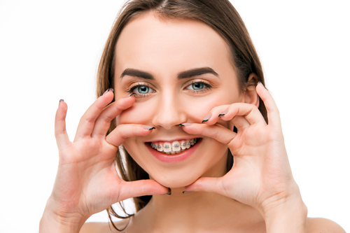 Beautiful young woman with teeth braces on gray